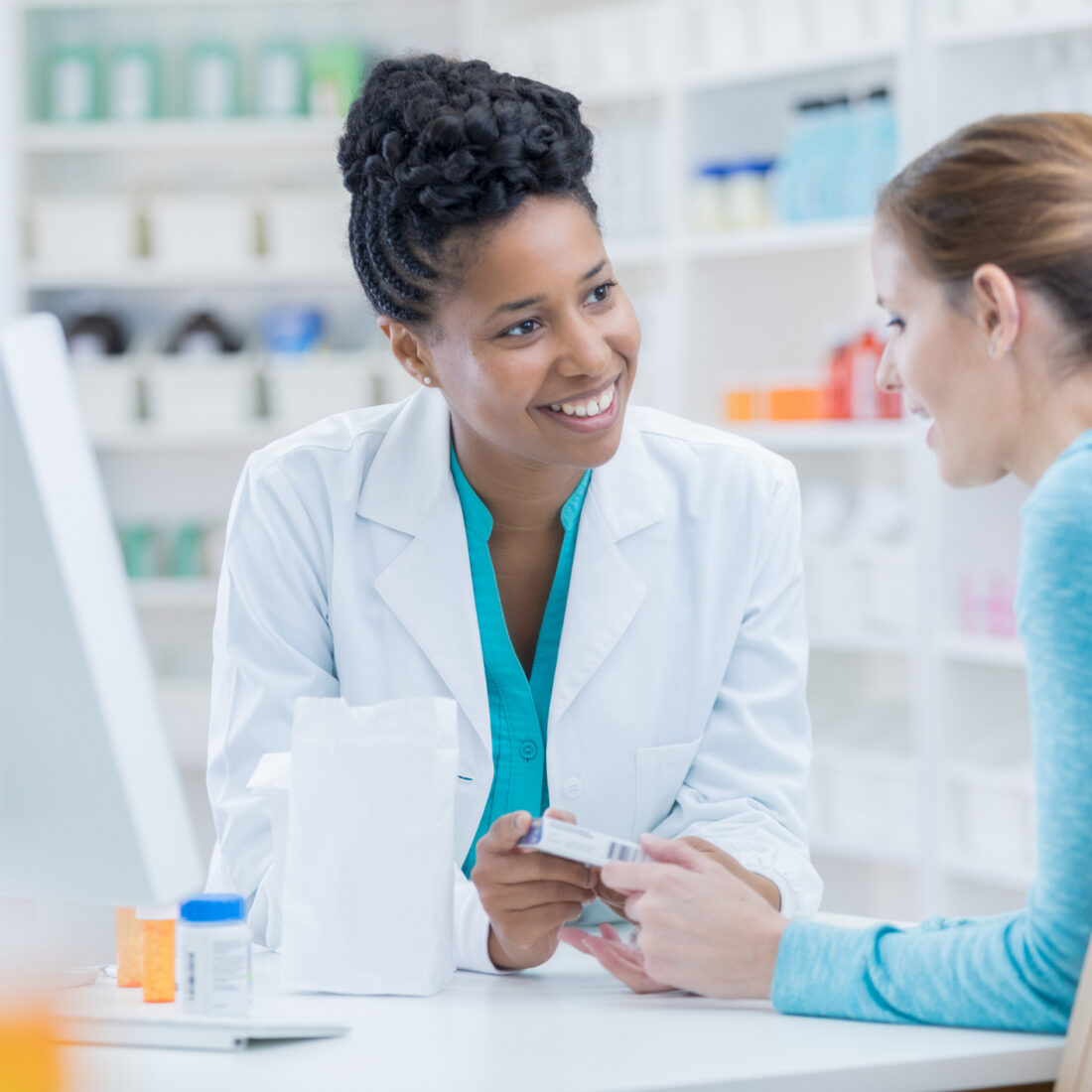 Mid adult female Caucasian pharmacy customer asks African American female pharmacist question about over the counter cold and flu medication.