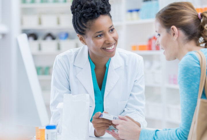 Mid adult female Caucasian pharmacy customer asks African American female pharmacist question about over the counter cold and flu medication.